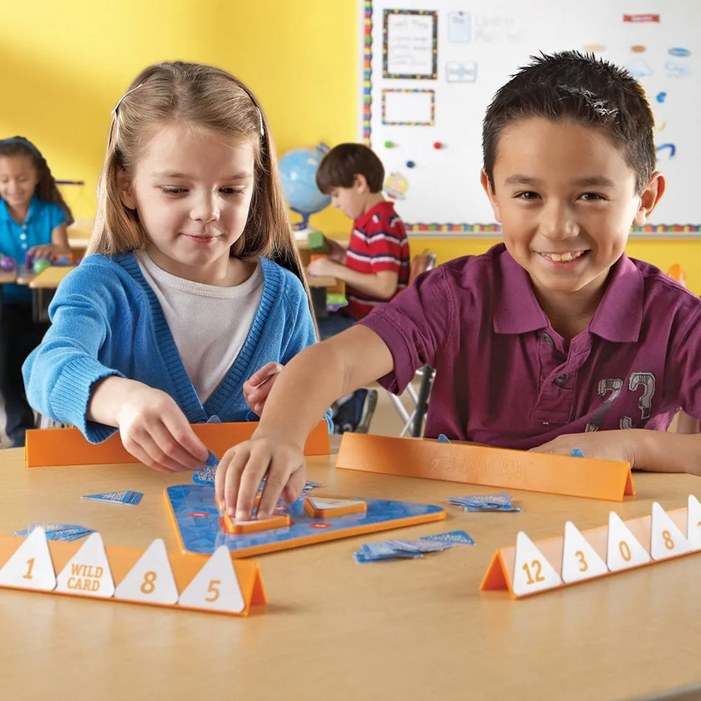 Two children playing a board game at a table with colorful game pieces and cards.