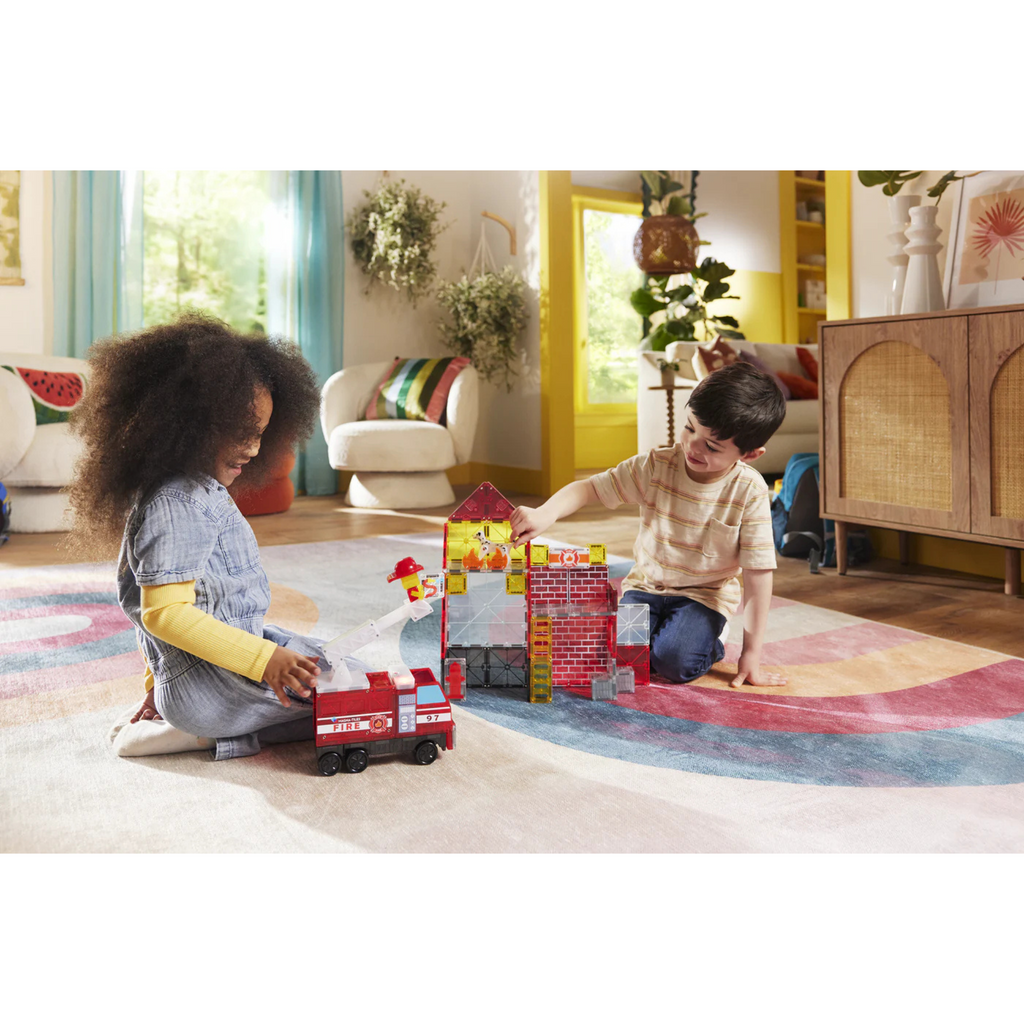 Two children playing with Fire Station MagnaTiles on a colorful rug in a living room.