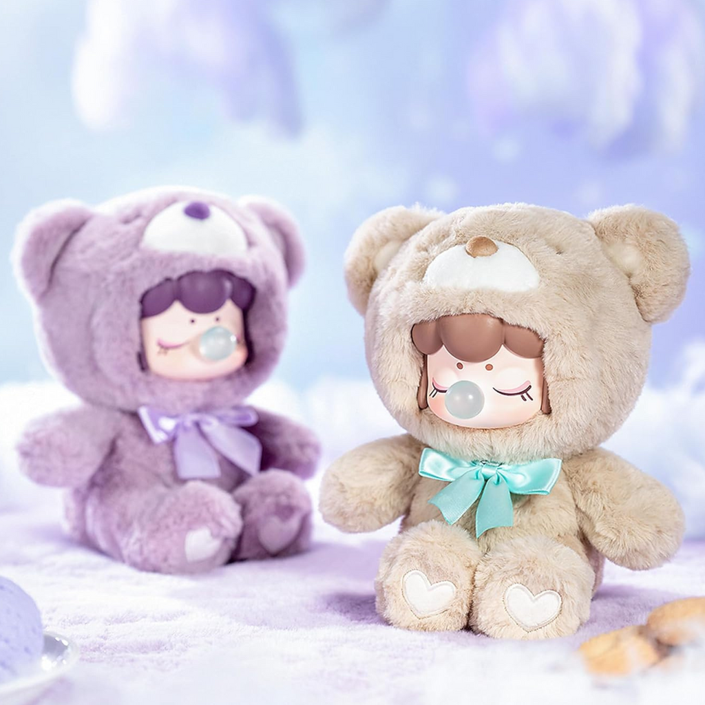 Two teddy bears, one purple and one beige, sitting on a soft surface with a blurred background.
