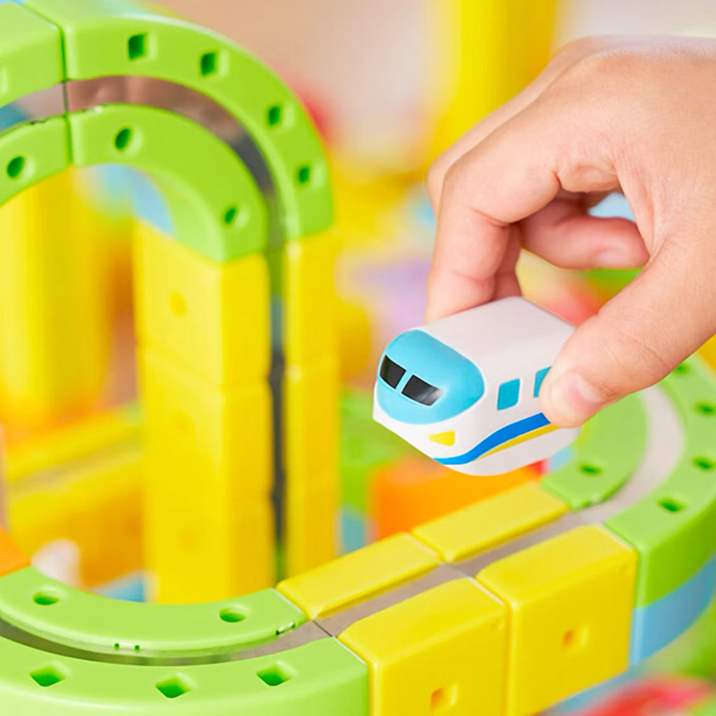 Toy train on a colorful track set with a hand placing the train on the tracks.