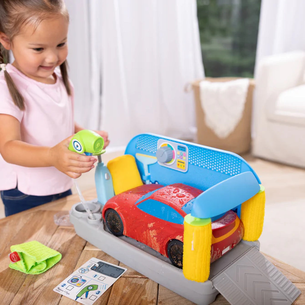 Child playing with a toy car wash set on a wooden table.