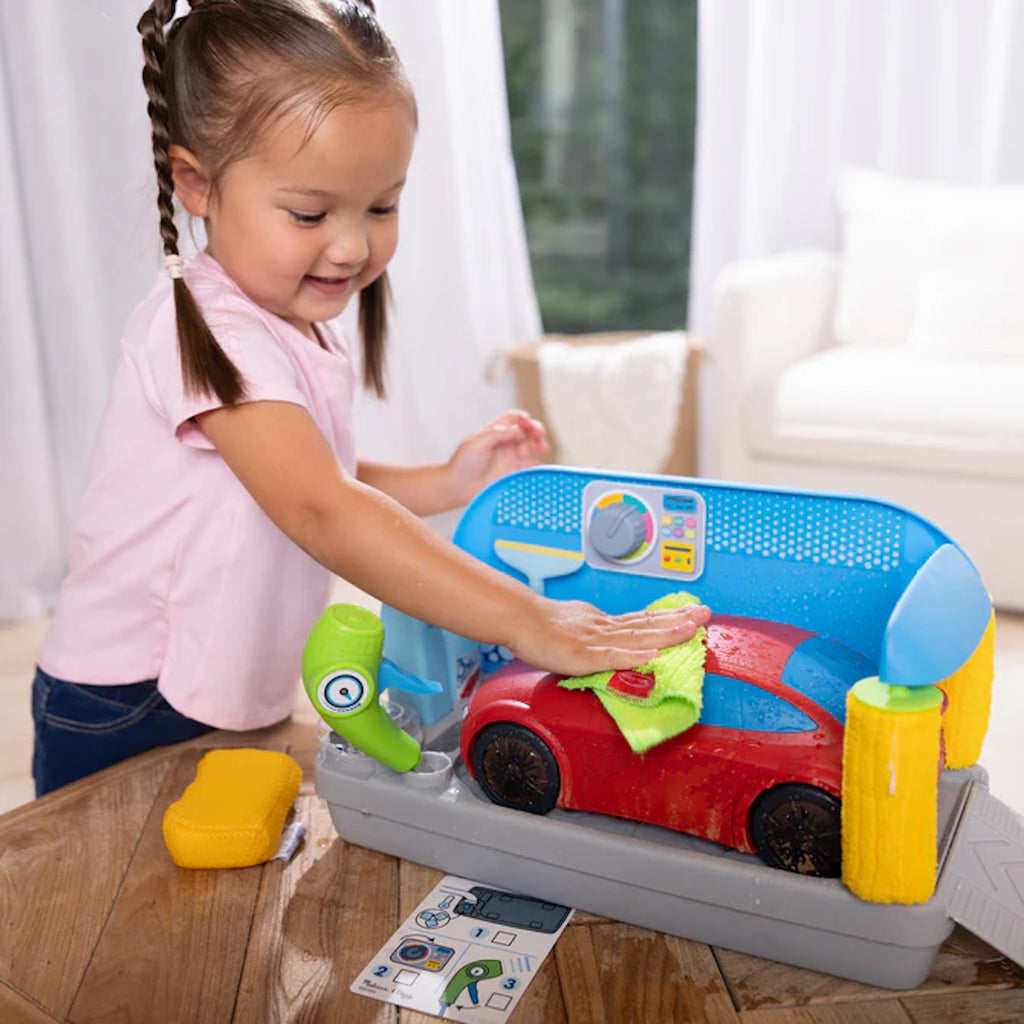 Child playing with a toy car wash set on a wooden table.