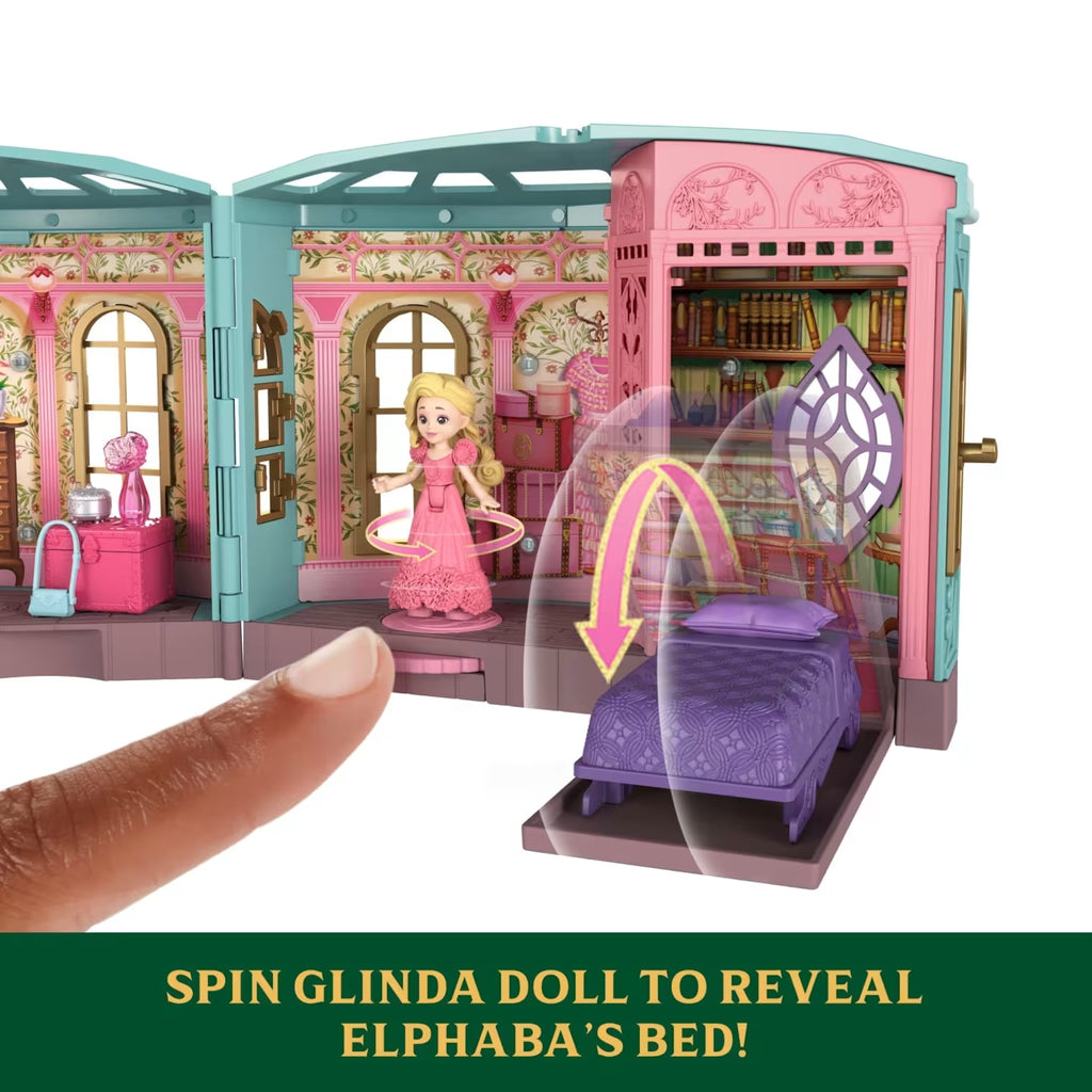 Toy dollhouse with a doll and a bed, featuring text 'Spin Glinda Doll to Reveal Elphaba's Bed'.