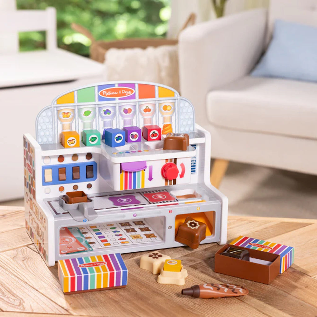 Colorful toy Chocolate Factory with accessories on a wooden floor in a living room setting.