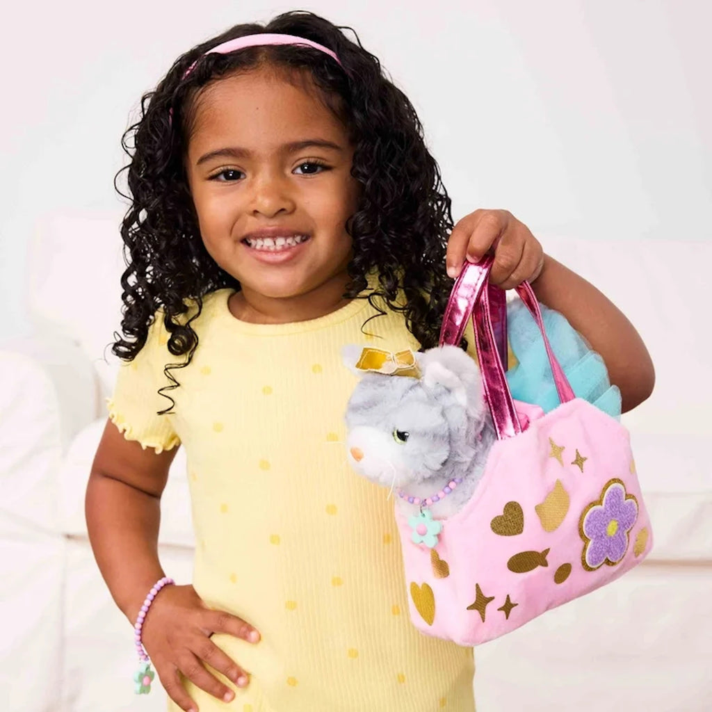 Young girl holding a pink decorated pet carrier with plush cat inside against a white background