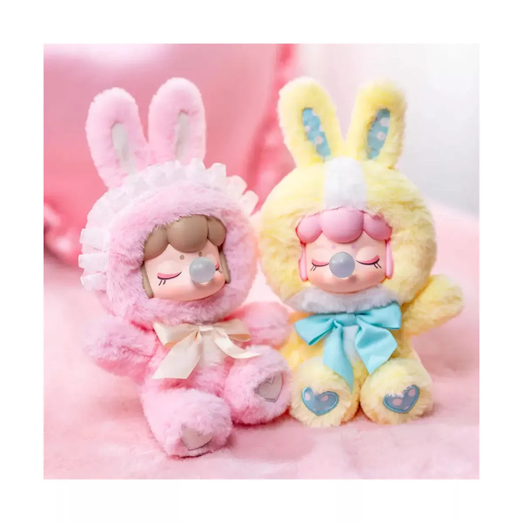 Two plush toys, one pink and one yellow, with bunny ears on a pink background.