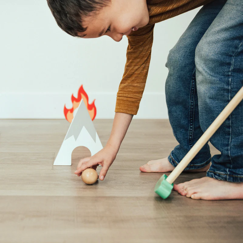 Child playing with a wooden ball and golf club on a wooden floor 