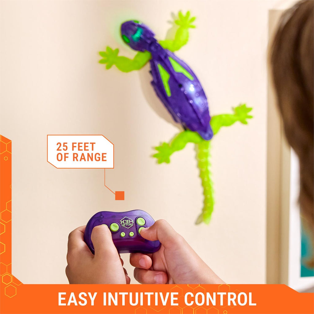 Purple and green toy gecko with remote control on a beige wall